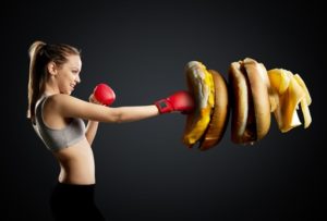 Fit, young, energetic woman boxing unhealthy food, black background